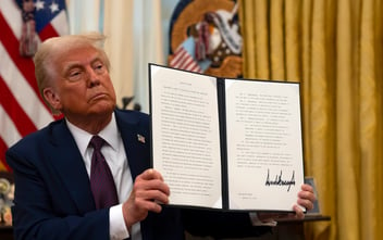 President Trump in the Oval Office holds up a document with his signature.