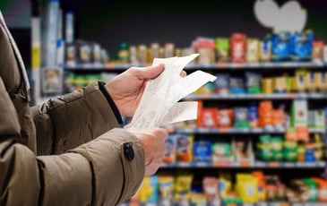 A person looks pensively at their receipt in a grocery store. 