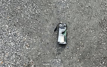 A broken and scorched pager lies on the pavement. It has clearly exploded recently. 