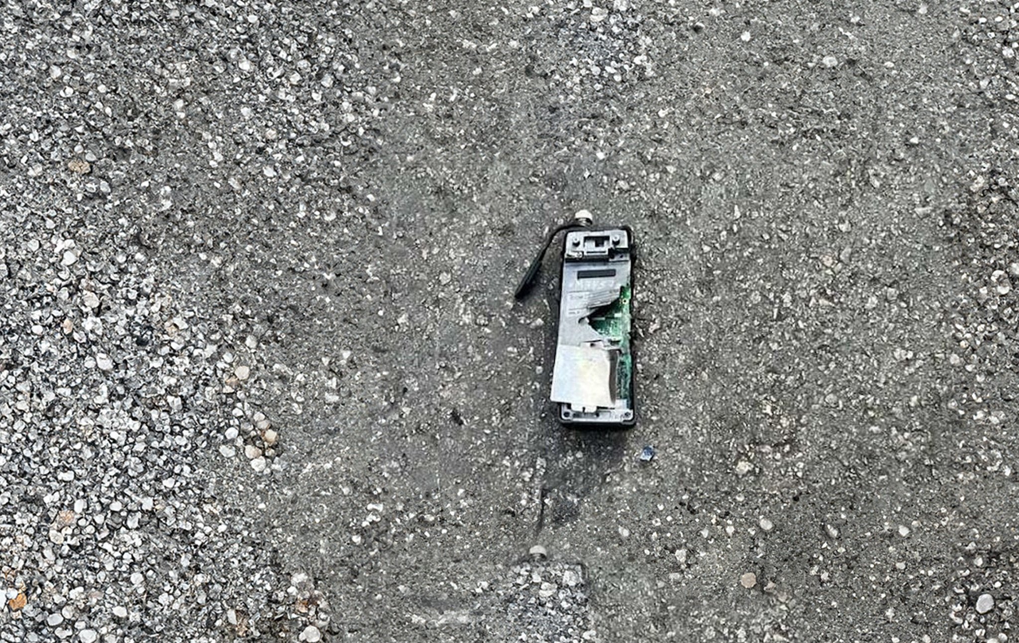 A broken and scorched pager lies on the pavement. It has clearly exploded recently. 